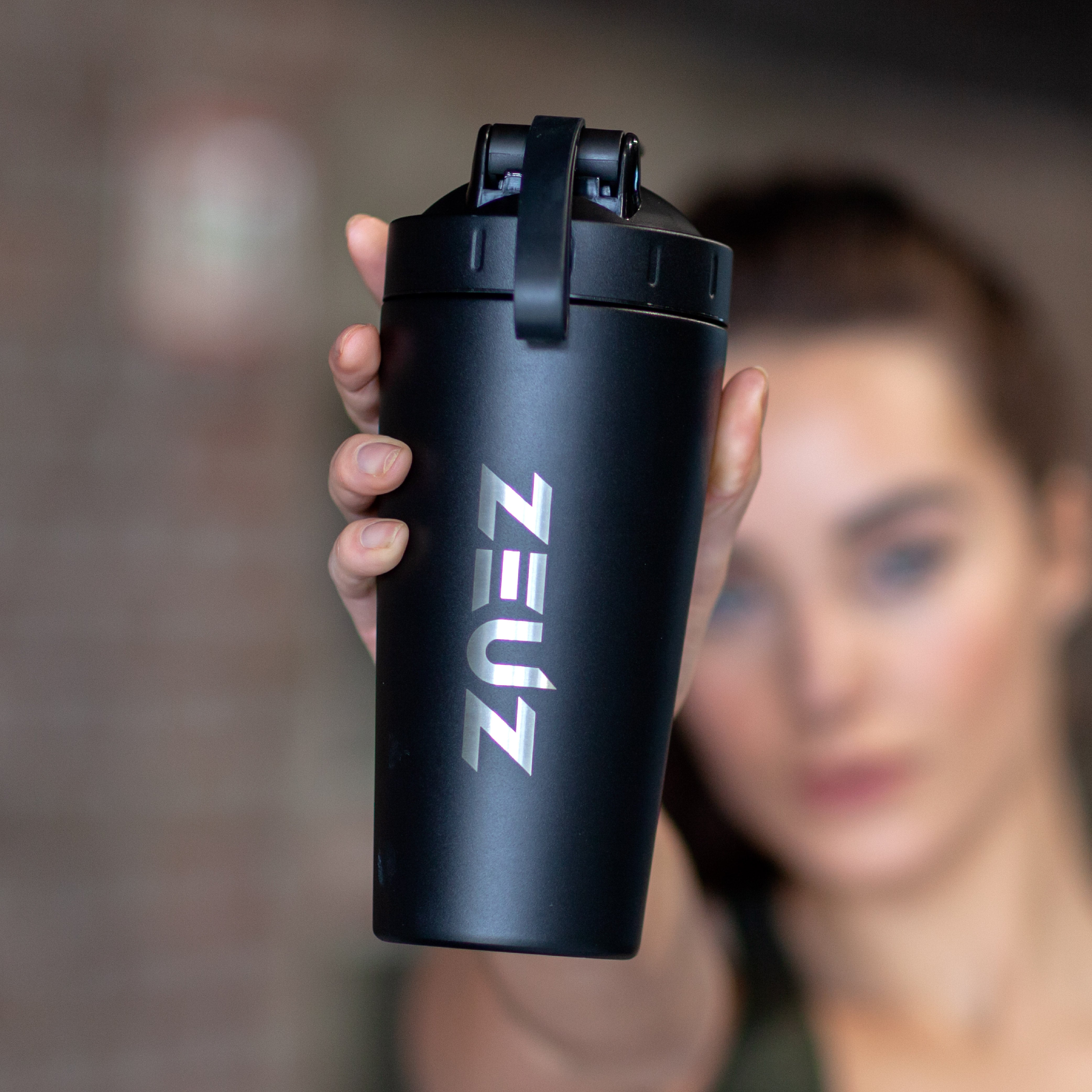 Vrouw gebruikt zwarte ZEUZ RVS shakebeker in de sportschool – stijlvolle en duurzame fitnessfles
