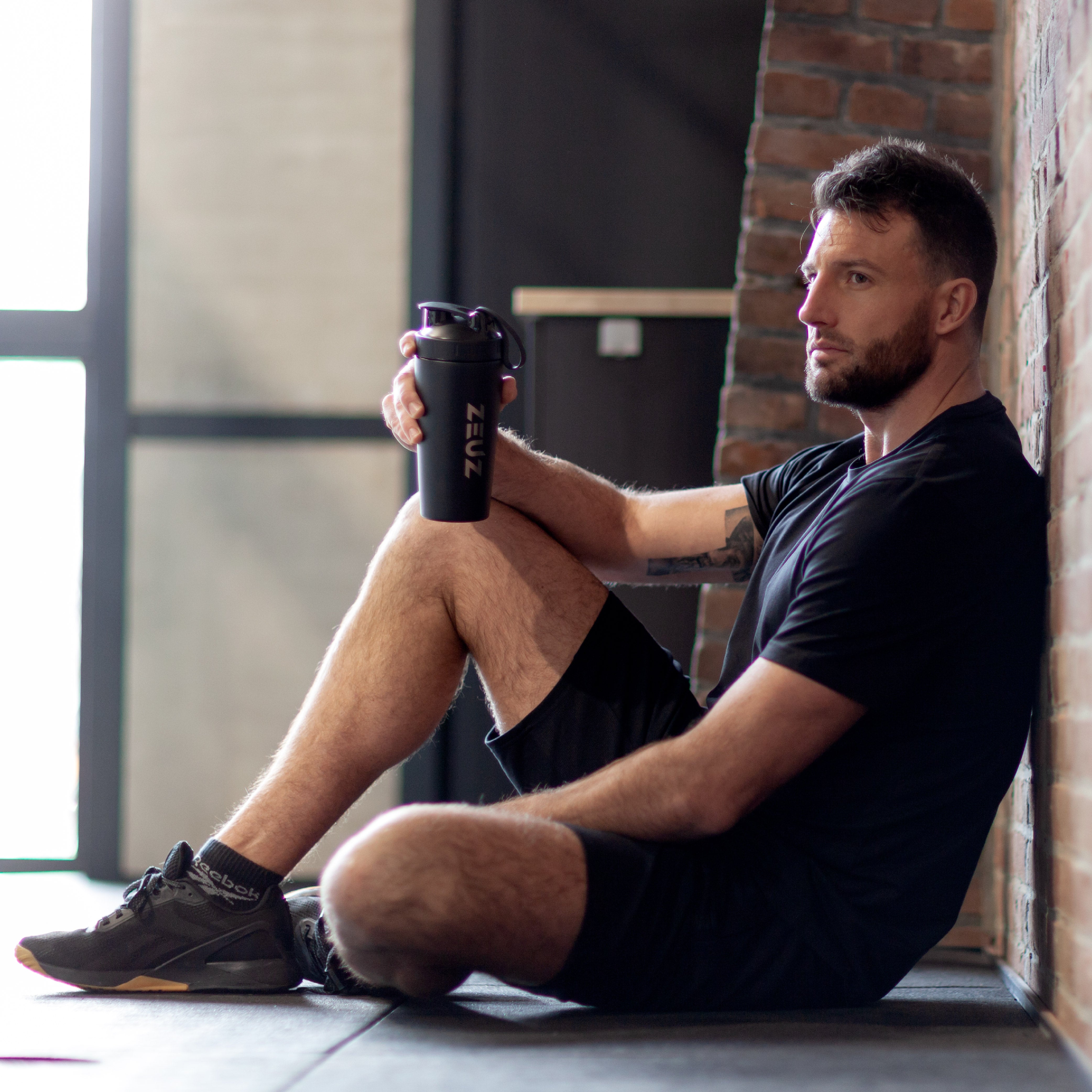Man met zwarte ZEUZ RVS shakebeker tijdens krachttraining – perfecte shaker voor sport en herstel
